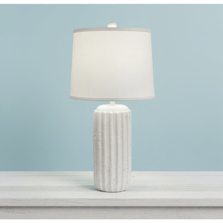 White textured table lamp with a white shade on a light gray surface against a light blue background