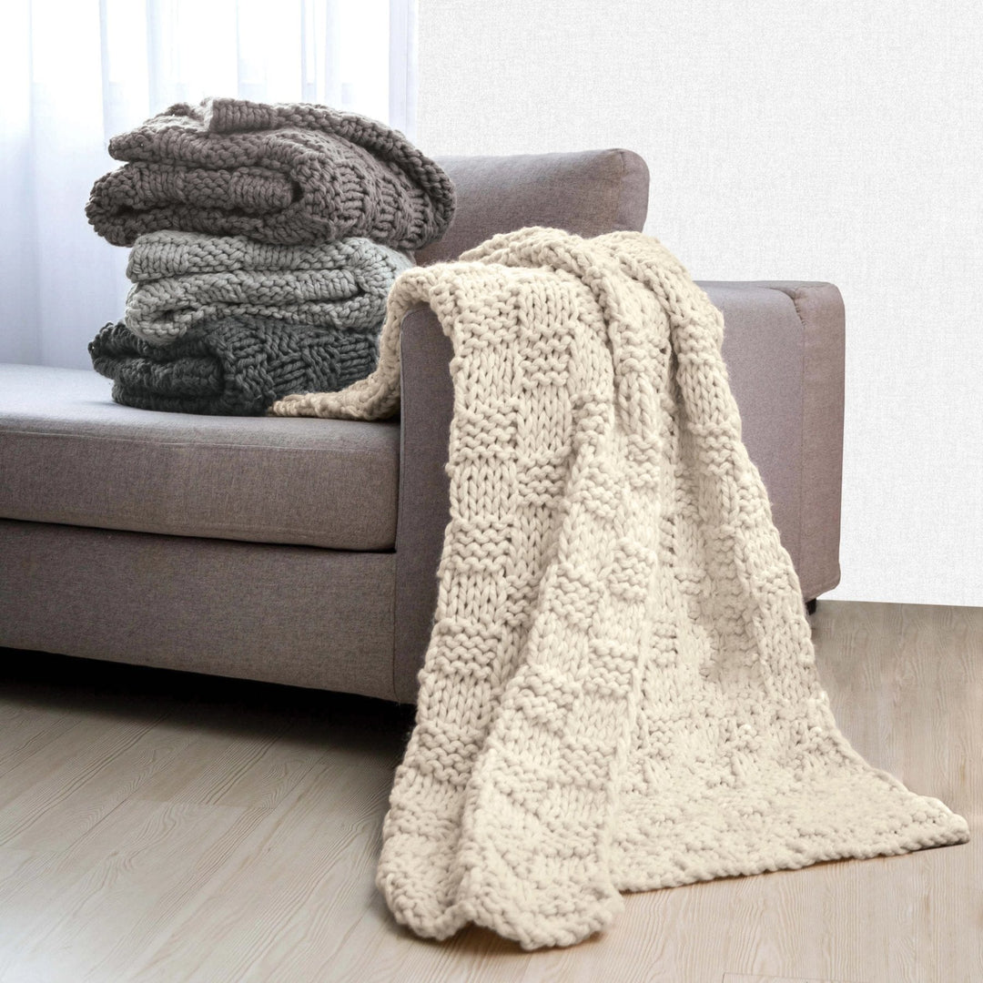 Stack of knitted blankets on a sofa in a living room setting - Coastal Compass Home Decor