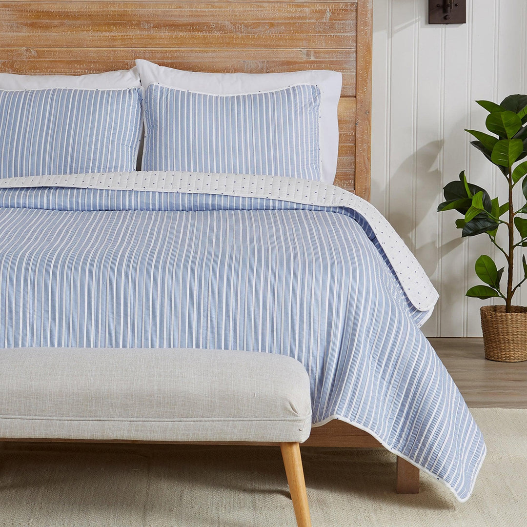 Bed with blue striped bedding and white pillows in a room with a wooden headboard and plant.