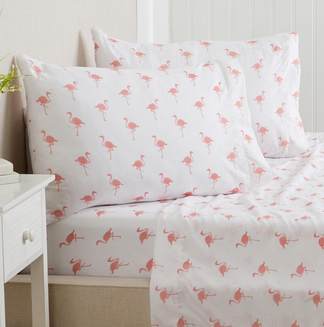 Flamingo-patterned bed sheets on a bed with a white nightstand.