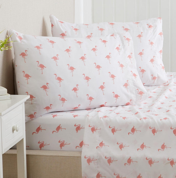 Flamingo-patterned bed sheets on a bed with a white nightstand.