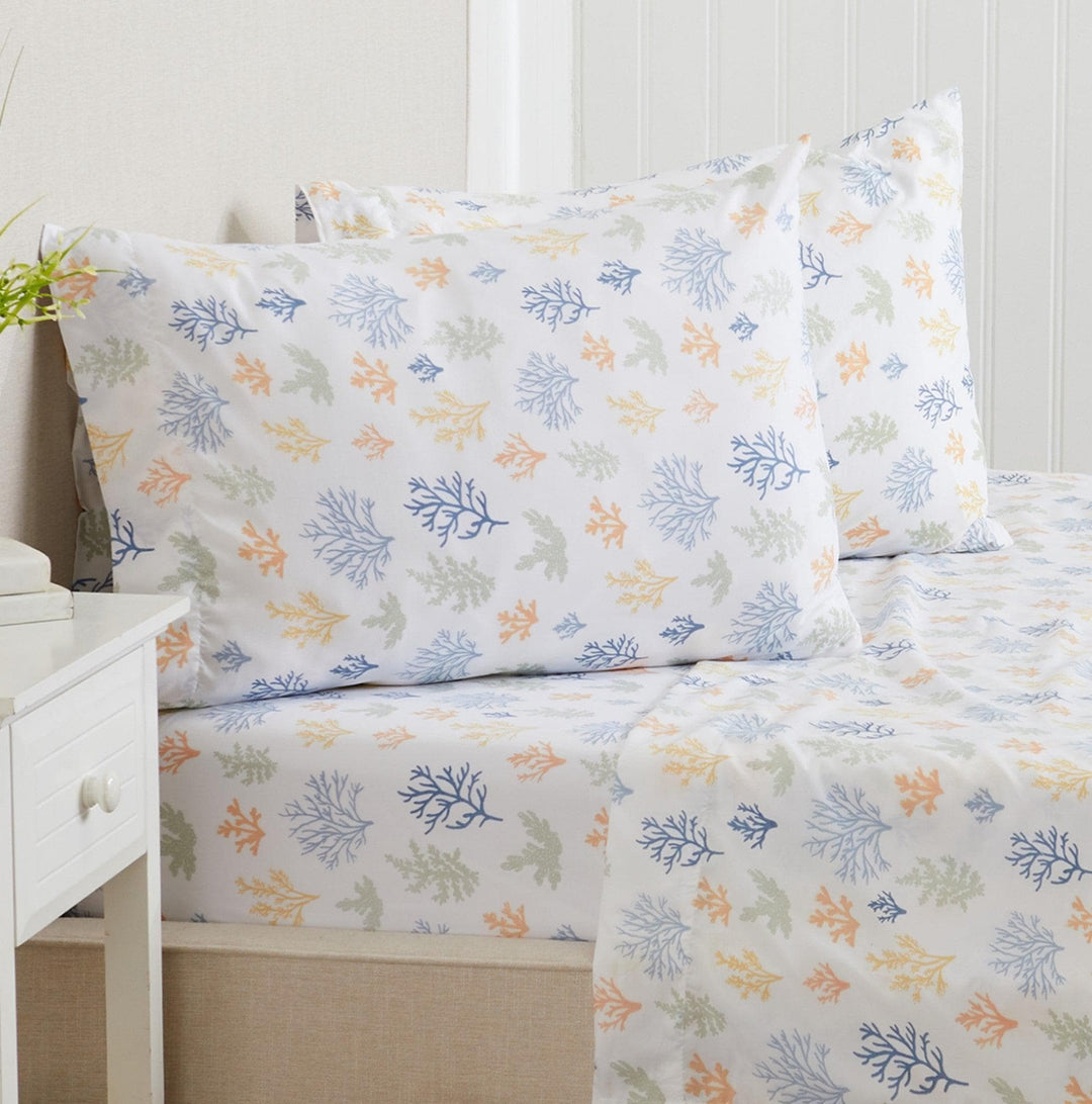 Coral reef patterned bed sheets and pillows on a bed with a white nightstand.