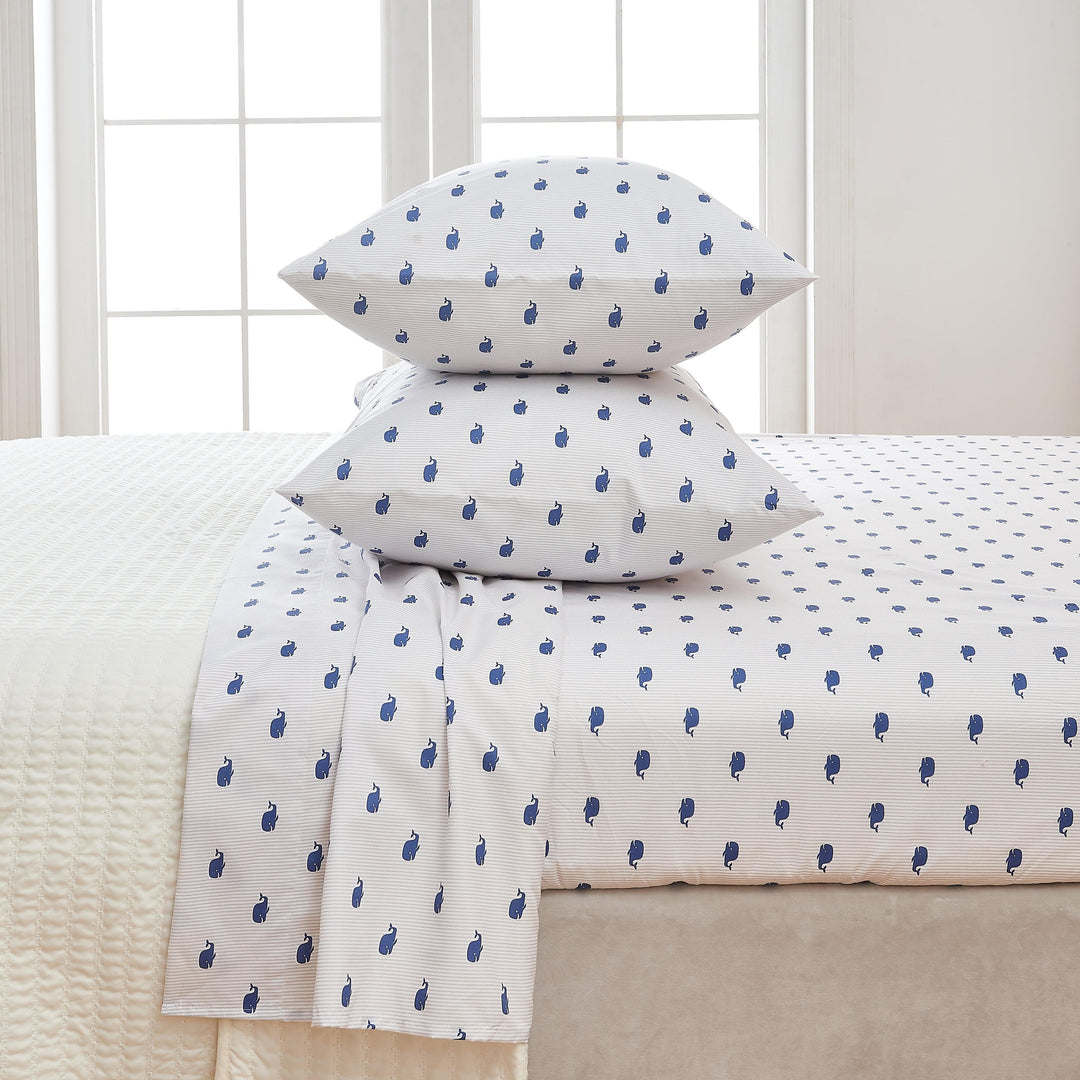 White bed sheets with blue whale pattern on a bed in a room with a window.