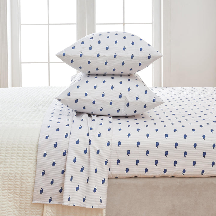 White bed sheets with blue whale pattern on a bed in a room with a window.