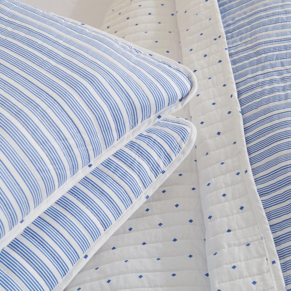 Blue and white striped bedding set with a quilt and pillows.