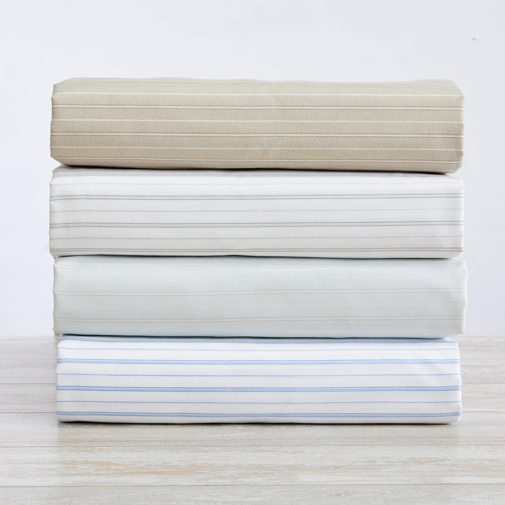 Stack of folded beige, white, and light blue bed sheets on a light wooden surface.