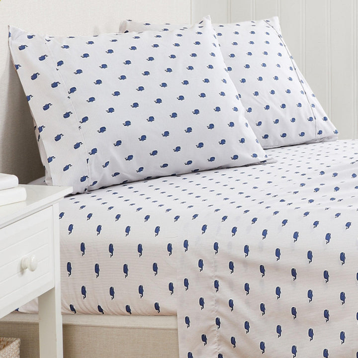 White bed sheets with blue whale pattern on a bed in a bedroom setting.