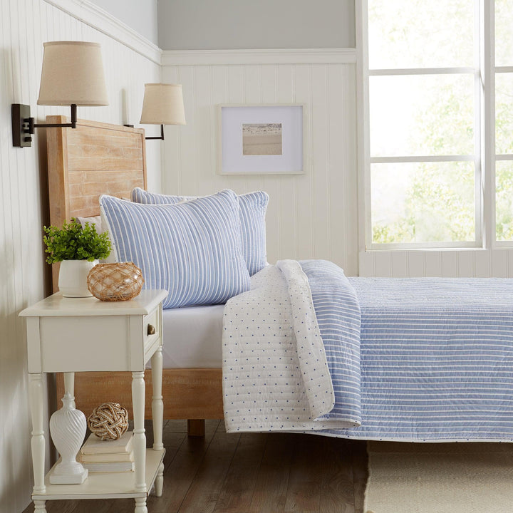 Bedroom with a bed featuring blue and white striped bedding, a wooden headboard, and a side table with decorative items.
