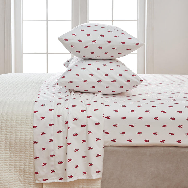 White bed sheets with red lobster pattern on a bed in a room with windows.