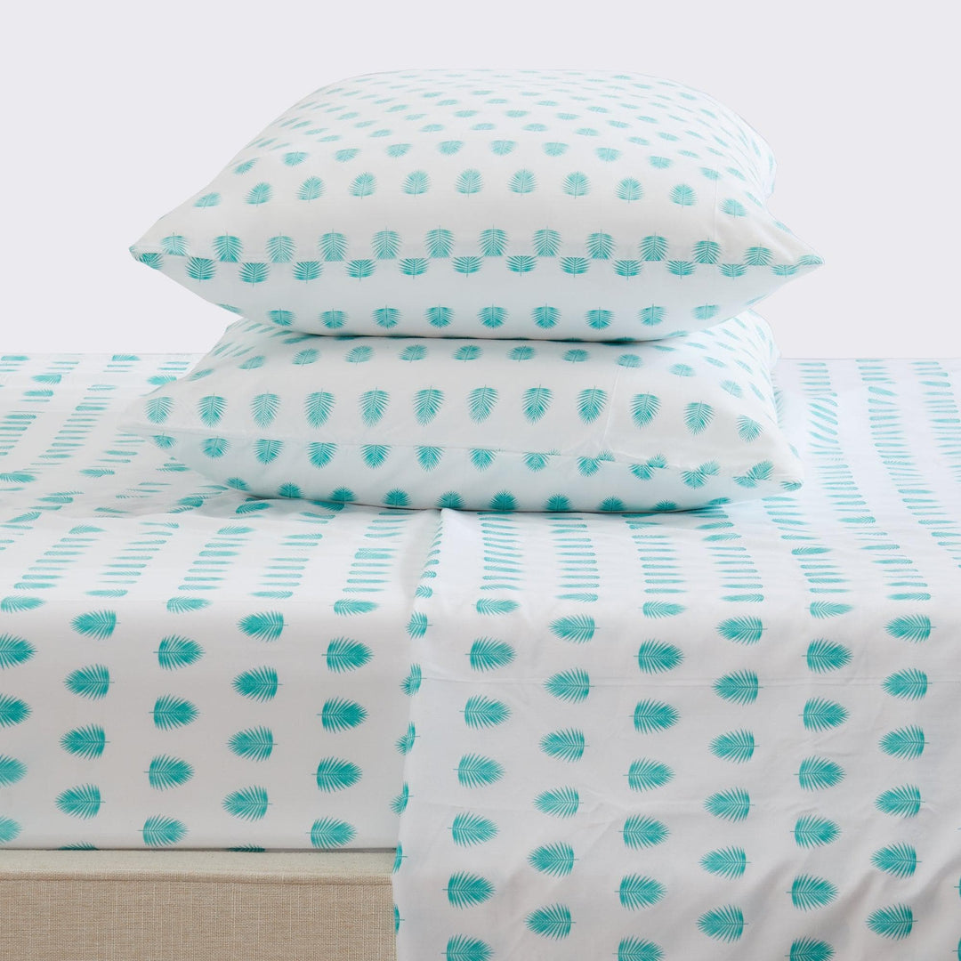 Teal and white tropical leaf patterned bedding set on a bed with pillows.
