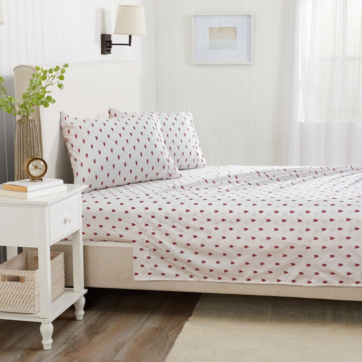 Bedroom with a bed featuring red lobster patterned sheetrs, nightstand, and decor items.