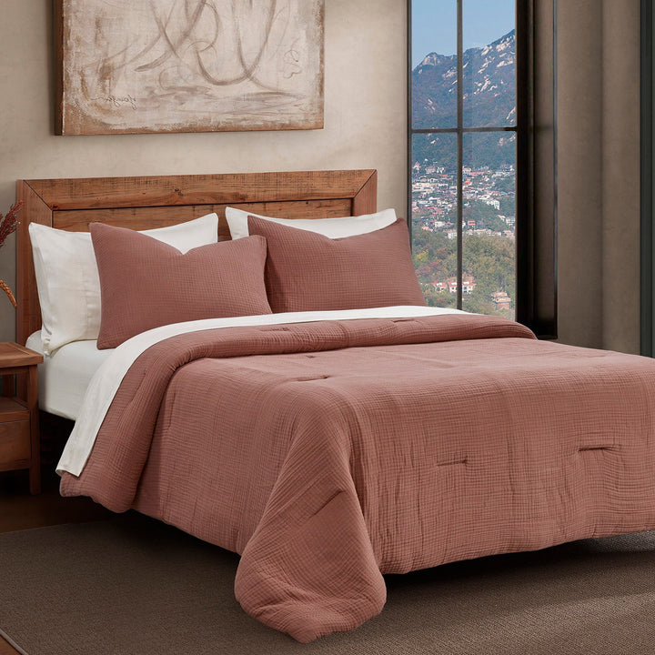 Voile cotton bedding set in Clay with comforter and pillows, next to a window with a mountain view